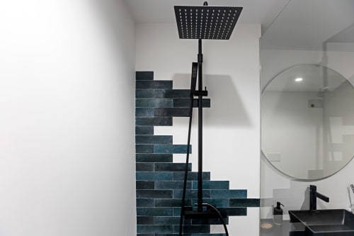 Modern bathroom in Porto studio with black rainfall showerhead, dark tile accent wall, round mirror, and black sink.