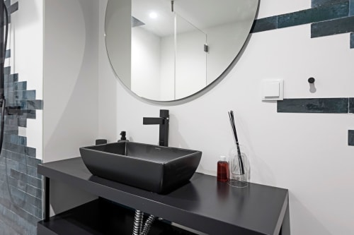 Modern bathroom in Porto hotel with black vessel sink, round mirror, and minimalist design with dark tile accents