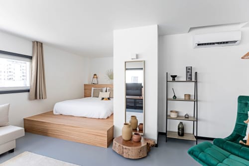 Estudio moderno y superior en Benefit Collection Porto con cama de madera, sillón de terciopelo verde, pequeña cocina y decoración minimalista