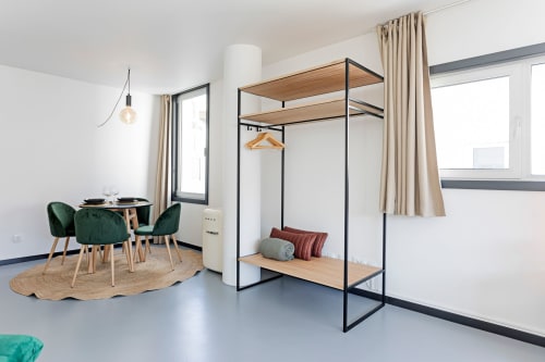 Moderno estudio superior en hotel Porto con zona de comedor, cama de estructura metálica negra, sillas verdes y cocina americana.