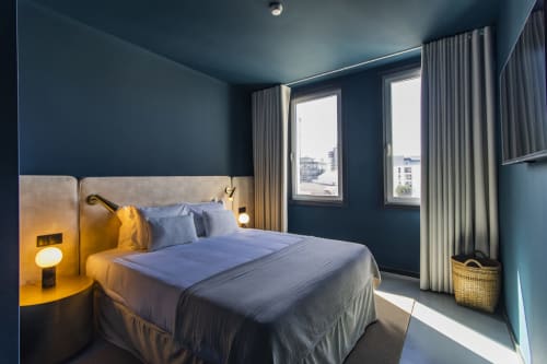 Modern bedroom in Porto hotel apartment with teal walls, beige headboard, blue bedding, and city views from floor-to-ceiling