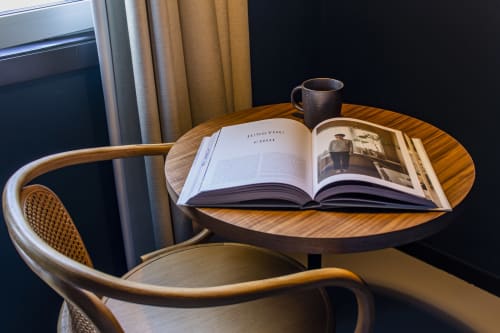 Wooden round table with open book and coffee mug in Porto hotel apartment, rattan chair in foreground