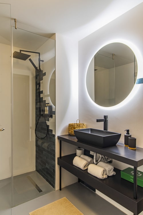 Modern bathroom in Porto hotel apartment with black vessel sink, LED mirror, glass shower enclosure, and black vanity with