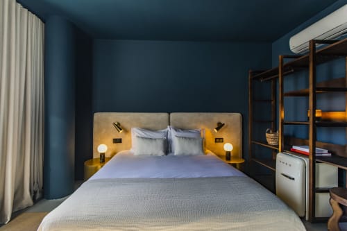 Modern Porto hotel bedroom with blue walls, queen bed, gold headboard, wooden shelving, and contemporary furnishings