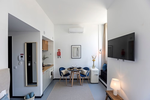 Estudio compacto en Oporto con mesa de comedor, sillas azules, cocina americana, televisor de pantalla plana y mobiliario moderno