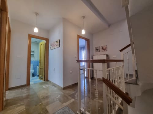 Bright hallway in Boabdil House cottage at CTH Granada, featuring wooden doors, staircase with railings, and tiled flooring