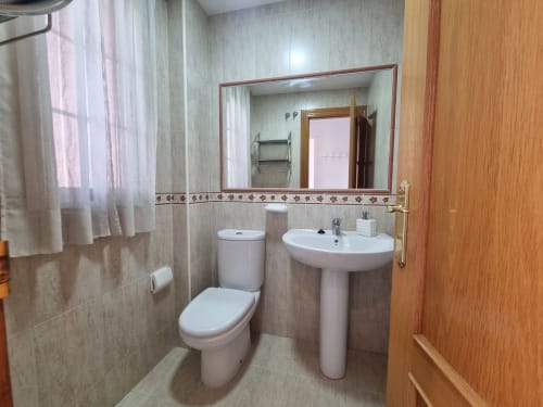 Modern bathroom in CTH Granada cottage with white pedestal sink, toilet, mirror, and tiled walls in Armilla, Granada