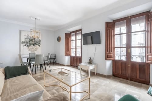 Salón moderno del apartamento en CTH Granada con sofá, comedor, televisor, puertas de madera y vistas a los monumentos de Granada