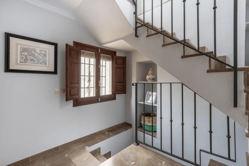 Escalera moderna con barandillas de metal en apartamento de Granada, con peldaños de madera, paredes blancas y nicho decorativo.
