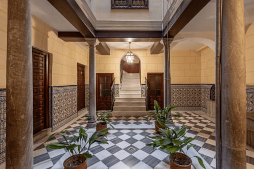 Elegante entrada al patio del CTH Granada con piso de azulejos a cuadros, columnas ornamentadas y plantas decorativas