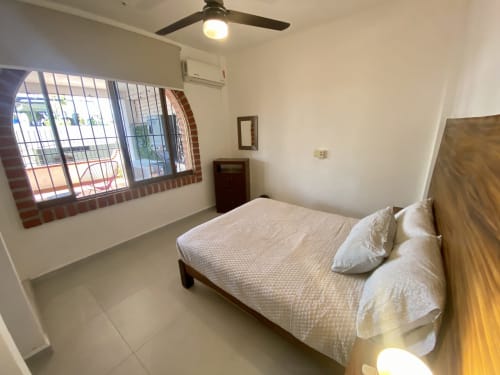 Bright bedroom at Anita Ocean View hotel in Puerto Vallarta with bed, ceiling fan, barred window, and sea view balcony access