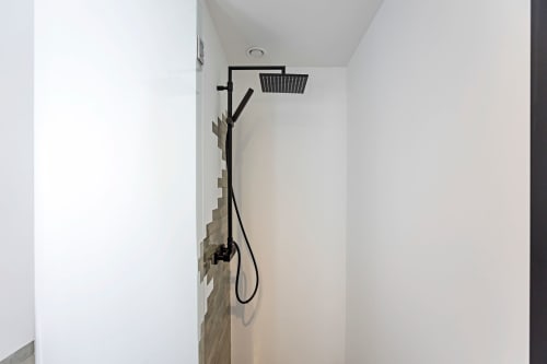 Moderno cabezal de ducha negro y ducha de mano en el baño contemporáneo del hotel Porto con paredes blancas y base alicatada.