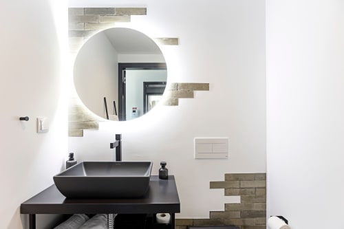 Baño moderno del hotel Benefit Collection Porto con espejo circular iluminado, lavabo negro y azulejos geométricos