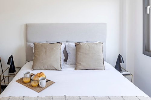 Cama compacta moderna con almohadas beige, sábanas blancas y bandeja de desayuno en habitación de hotel en Oporto