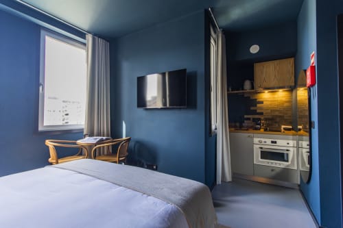 Estudio compacto y moderno en Oporto con paredes azules, cama, cocina americana con horno, televisión pantalla plana y luz natural