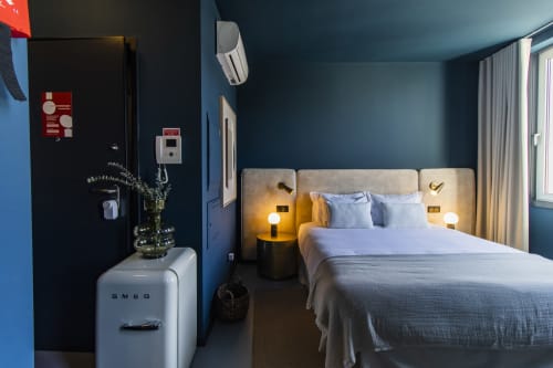 Modern hotel room in Porto with blue walls, bed with cream headboard, white SMEG refrigerator, and garden view curtains