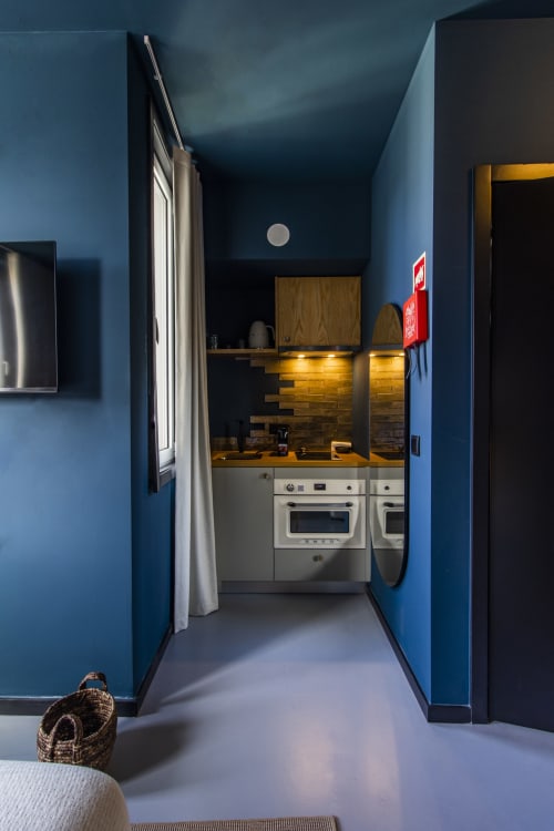 Pequeña cocina moderna en habitación de hotel en Oporto con paredes azules, gabinetes blancos, encimeras doradas y electrodomésticos de acero inoxidable