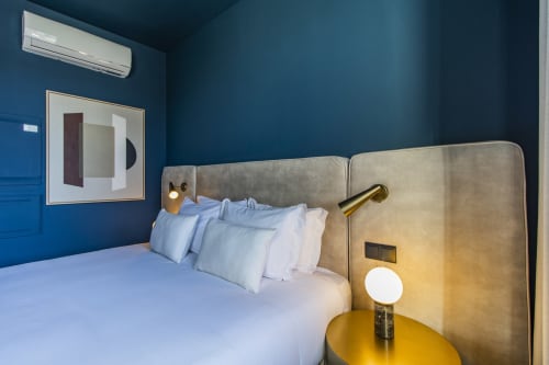 Moderno estudio dormitorio compacto en Oporto con paredes color azul verdoso, cama tapizada beige, accesorios de latón y ropa de cama blanca