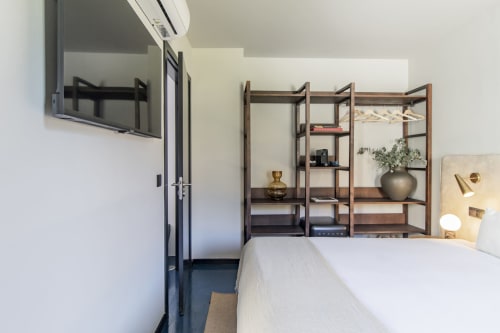Modern compact studio bedroom in Porto hotel with white bed, wooden shelving unit, TV, and minimalist decor