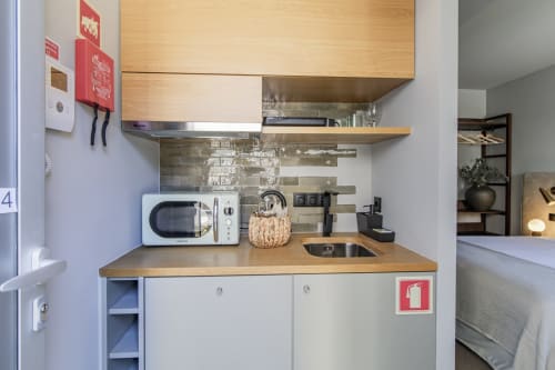 Kitchenette compacte à l'hôtel Benefit Collection Porto avec micro-ondes, cuisinière, évier et rangements en bois