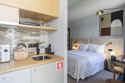Studio compacto no Porto com kitchenette, cama com cabeceira bege, prateleiras de madeira e móveis modernos