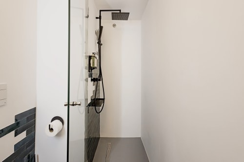 Banheiro moderno do apartamento no Porto no hotel Benefit Collection com acabamentos pretos, chuveiro tipo chuva, box de vidro