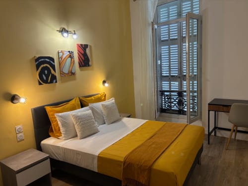 Chambre double moderne à l'Hôtel Manon à Marseille avec murs jaunes, literie dorée et œuvres d'art contemporain