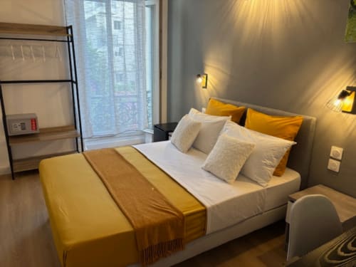 Modern double bedroom at Hôtel Manon in Marseille with yellow accents, white bedding, and contemporary lighting