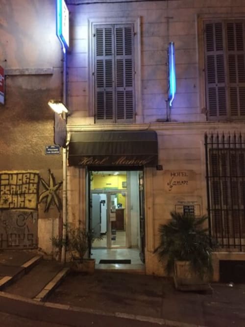 Façade de l'Hôtel Manon la nuit à Marseille, illuminée en bleu néon avec volets fermés