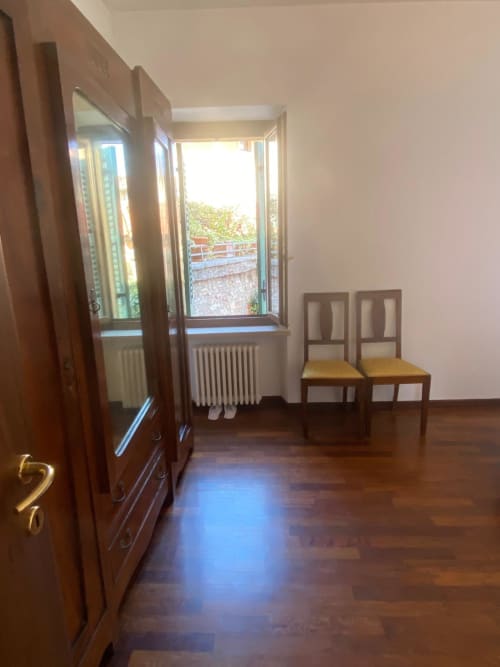 Bedroom at Alloggio Le Casette in Verona with wooden wardrobe, chairs, and garden view through open window