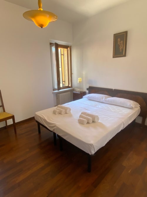 Modern bedroom at Alloggio Le Casette in Verona with white bedding, dark wood frame, golden ceiling lamp, and wooden flooring