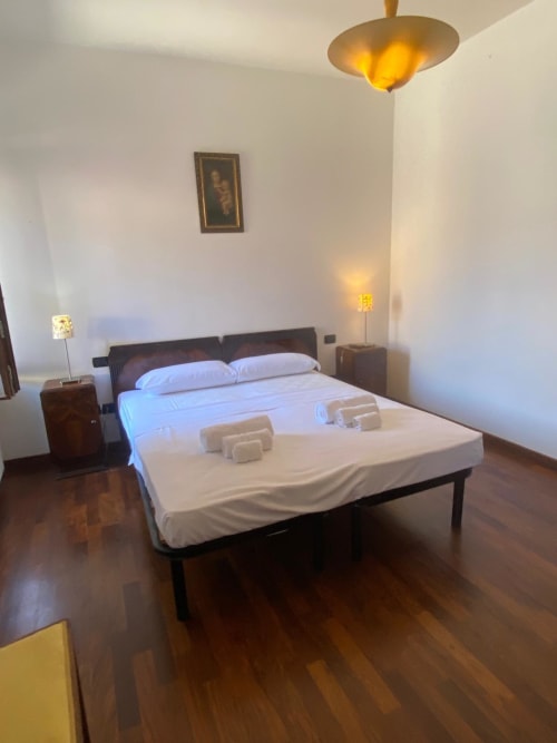 Modern bedroom at Alloggio Le Casette in Verona with queen bed, white linens, dark wood flooring, and warm lighting