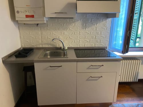 Compact kitchenette with sink, stovetop, white cabinetry, and brick backsplash in Verona apartment