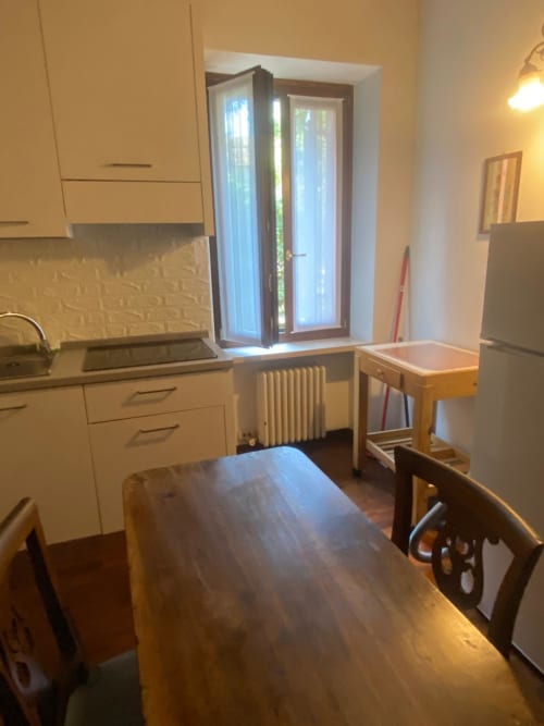 Bright kitchen and dining area in Verona apartment with white cabinets, wooden table, and garden view through glass doors