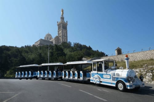 Blue and white tourist train at Basilica of Notre-Dame de la Garde in Marseille near Hôtel Manon