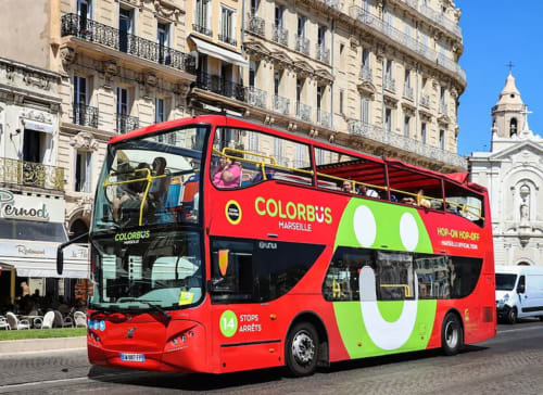 Red Colorbus hop-on hop-off tour bus in Marseille with historic Haussmann buildings and church in background