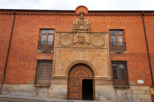 Fachada histórica de edificio de ladrillo rojo en el centro de Benavente con puerta de madera ornamentada y detalles decorativos de piedra