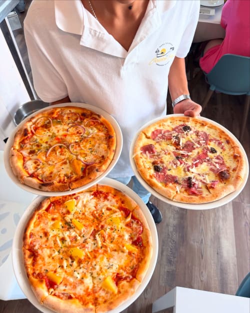 Server at Costa Alentejana holding three fresh pizzas at Zambujeira do Mar restaurant