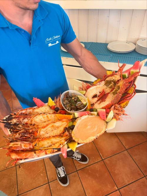 Staff member at Costa Alentejana displaying fresh seafood platter with lobster, prawns, and clams in Zambujeira do Mar