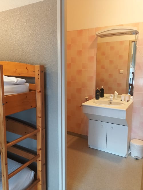 Salle de bain à la Résidence Soansa du Gérardmer : vasque blanche, miroir, carrelage orange et rangements en bois