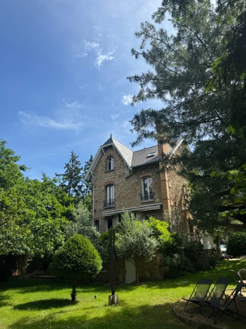 Villa Saint-Hilaire in Colombes with stone facade, manicured gardens, and deck chairs under blue sky