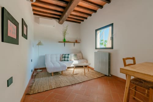 Accogliente soggiorno a Tenuta Alela con divano bianco, travi in legno, pavimento in cotto e vista sul giardino