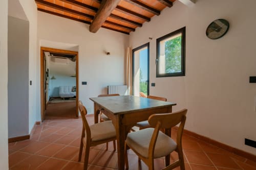 Zona pranzo nell'appartamento deluxe di Tenuta Alela con tavolo in legno, sedie, pavimenti in cotto, travi a vista e vista sul giardino