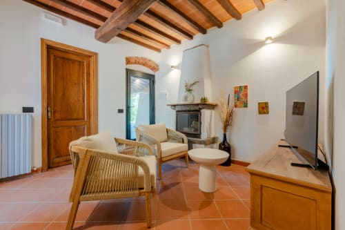 Elegante soggiorno a Tenuta Alela con pavimenti in terracotta, travi in legno, camino, sedie in rattan e vista sulla piscina