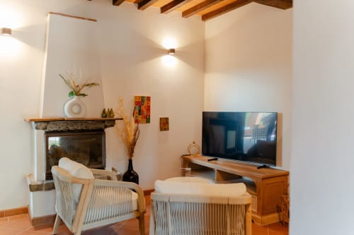 Soggiorno moderno a Tenuta Alela con camino, due poltrone imbottite, TV a schermo piatto, travi in legno e stile elegante