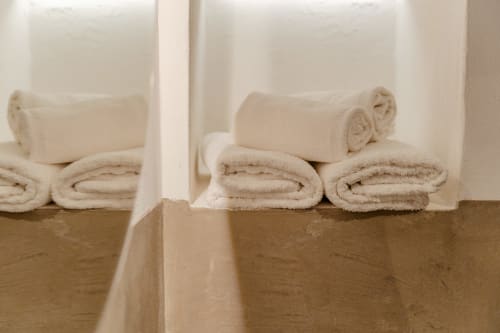 Asciugamani in crema arrotolati ordinatamente disposti su uno scaffale bianco nell'Apartment Deluxe di Tenuta Alela, Figline Valdarno