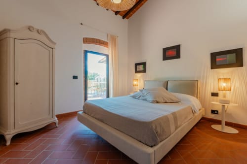 Camera da letto in Camino Apartment a Tenuta Alela con letto queen, armadio bianco, pavimenti in cotto, balcone con vista piscina e