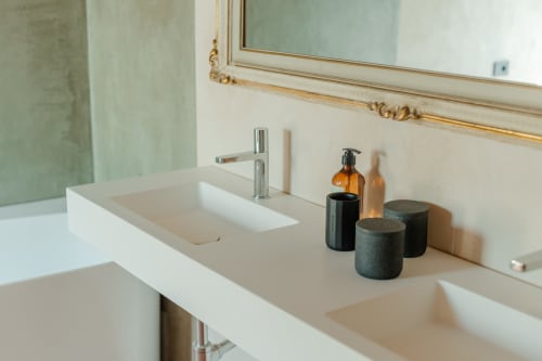 Vanity bagno moderno a Tenuta Alela con doppi lavabi, rubinetteria cromata, bottiglie ambrate e accessori neri su sfondo crema