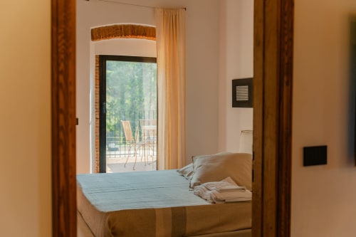 Camera da letto in Camino Apartment presso Tenuta Alela con vista giardino, letto e accesso al balcone affacciato sulla terrazza