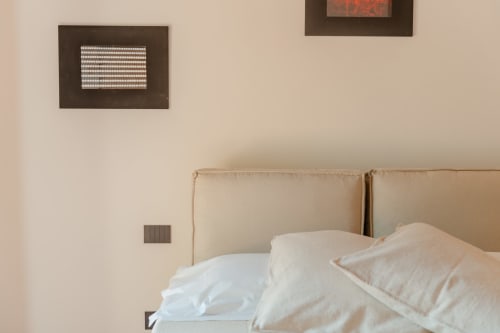 Letto rivestito in beige con cuscini bianchi nell'Appartamento Camino di Tenuta Alela, Figline Valdarno, con quadri incorniciati su parete crema